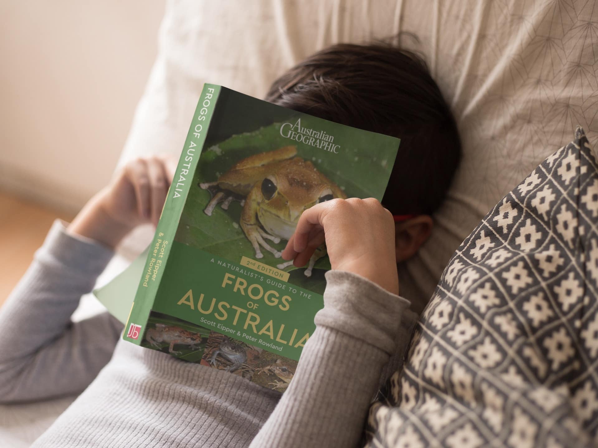 A shy girl reading A Naturalist's Guide to the Frogs of Australia by Scott Eipper and Peter Rowland